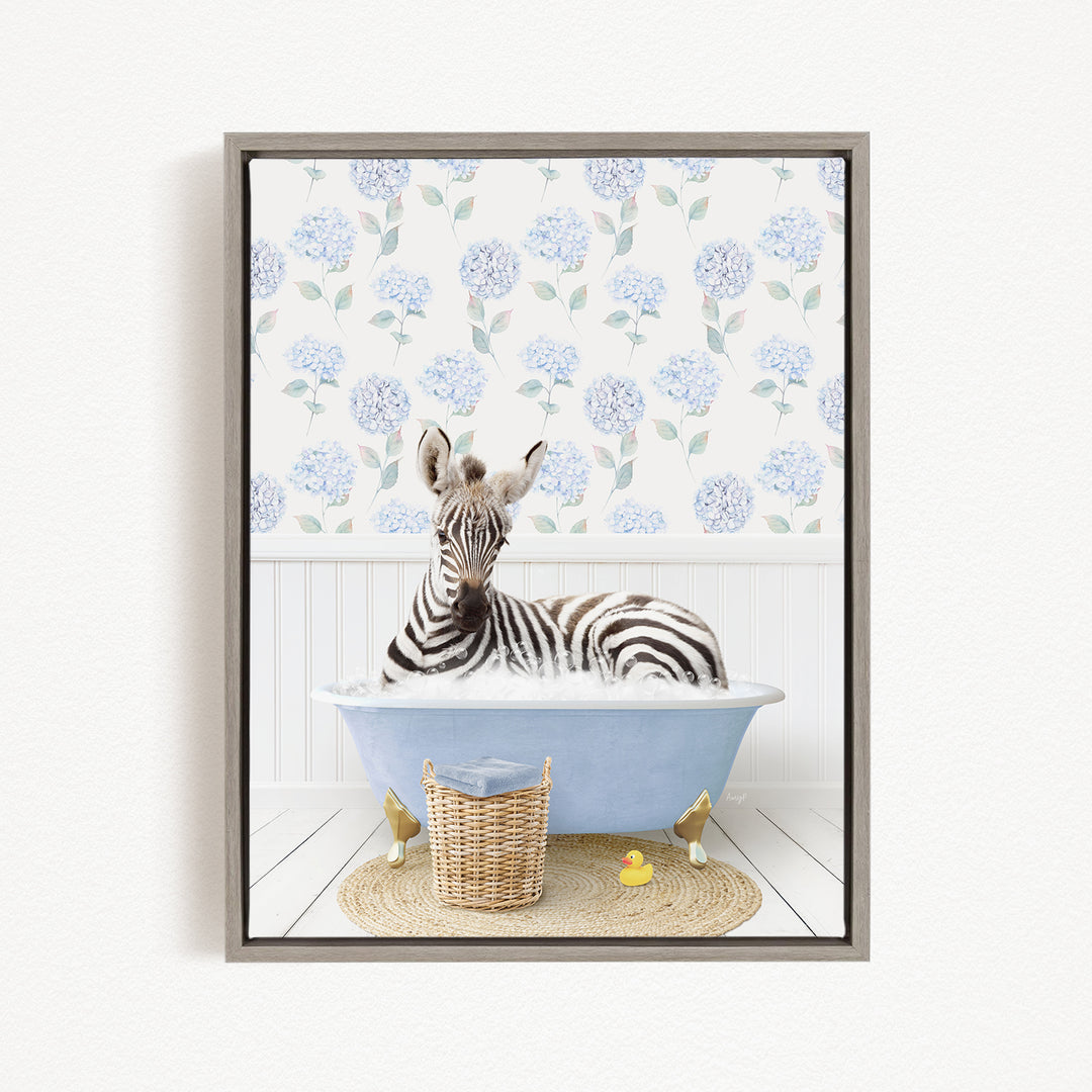 A zebra is sitting in a blue bathtub filled with water, surrounded by a wicker basket and a rubber duck.