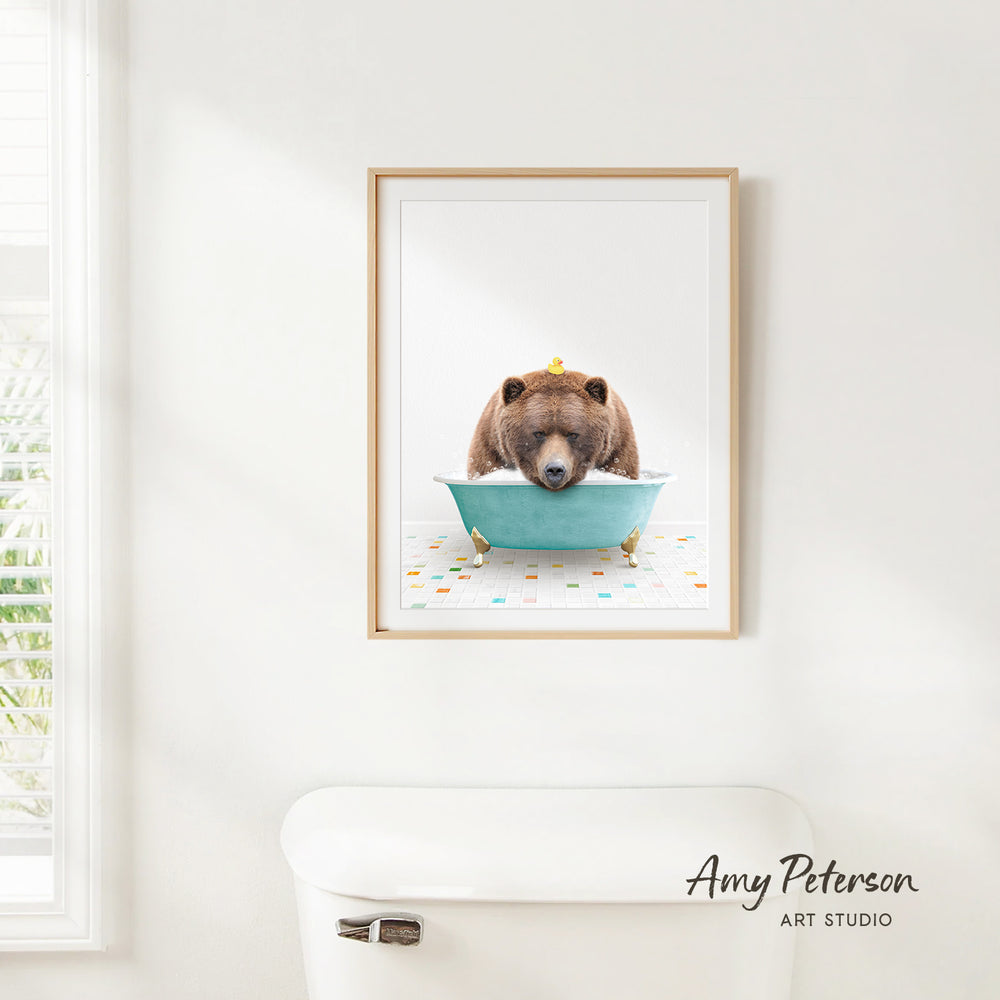A framed image of a brown bear sitting in a blue bathtub, with a yellow rubber duck floating on the water.