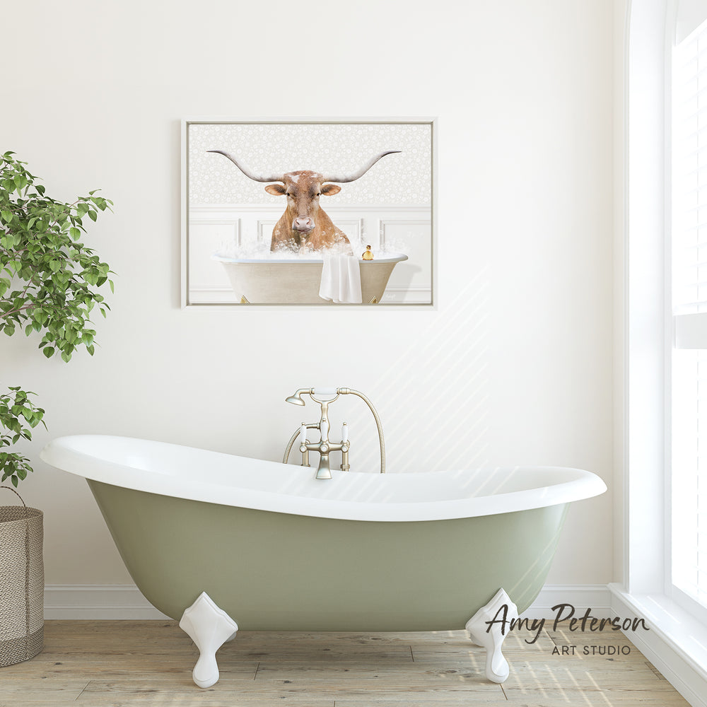 A framed image of a bull with long horns is displayed on the wall above a green clawfoot bathtub in a bright, white bathroom.