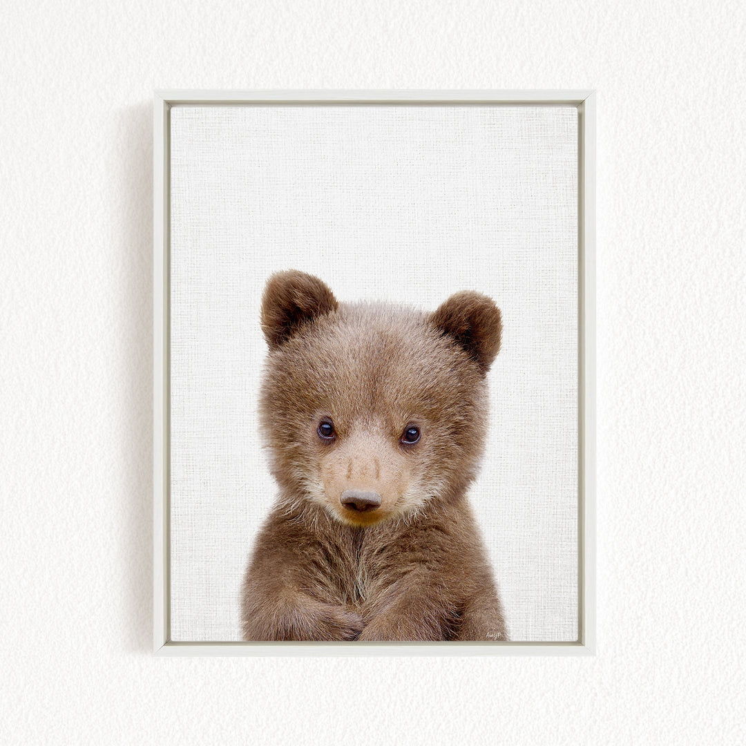 A cute brown bear cub with large eyes and a curious expression is the focus of the image.