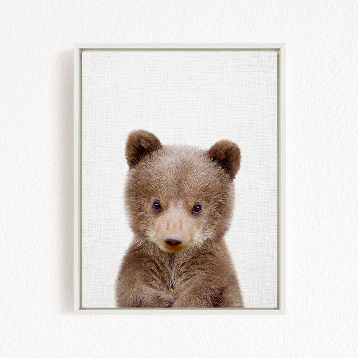 A cute brown bear cub with large eyes and a curious expression is the focus of the image.