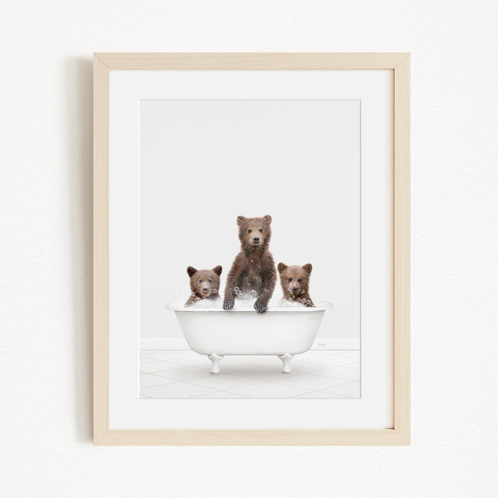 A framed image depicting three brown bears sitting in a white bathtub.