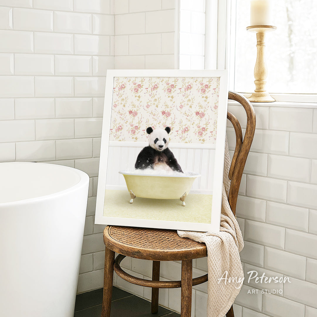 A framed image of a panda bear sitting in a bathtub, surrounded by a floral pattern, is displayed on a wooden chair in a bathroom setting.