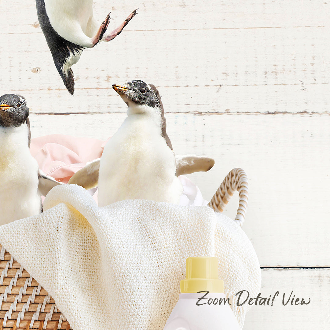 A group of penguins standing in a basket filled with laundry, including a white cloth and a yellow bottle.