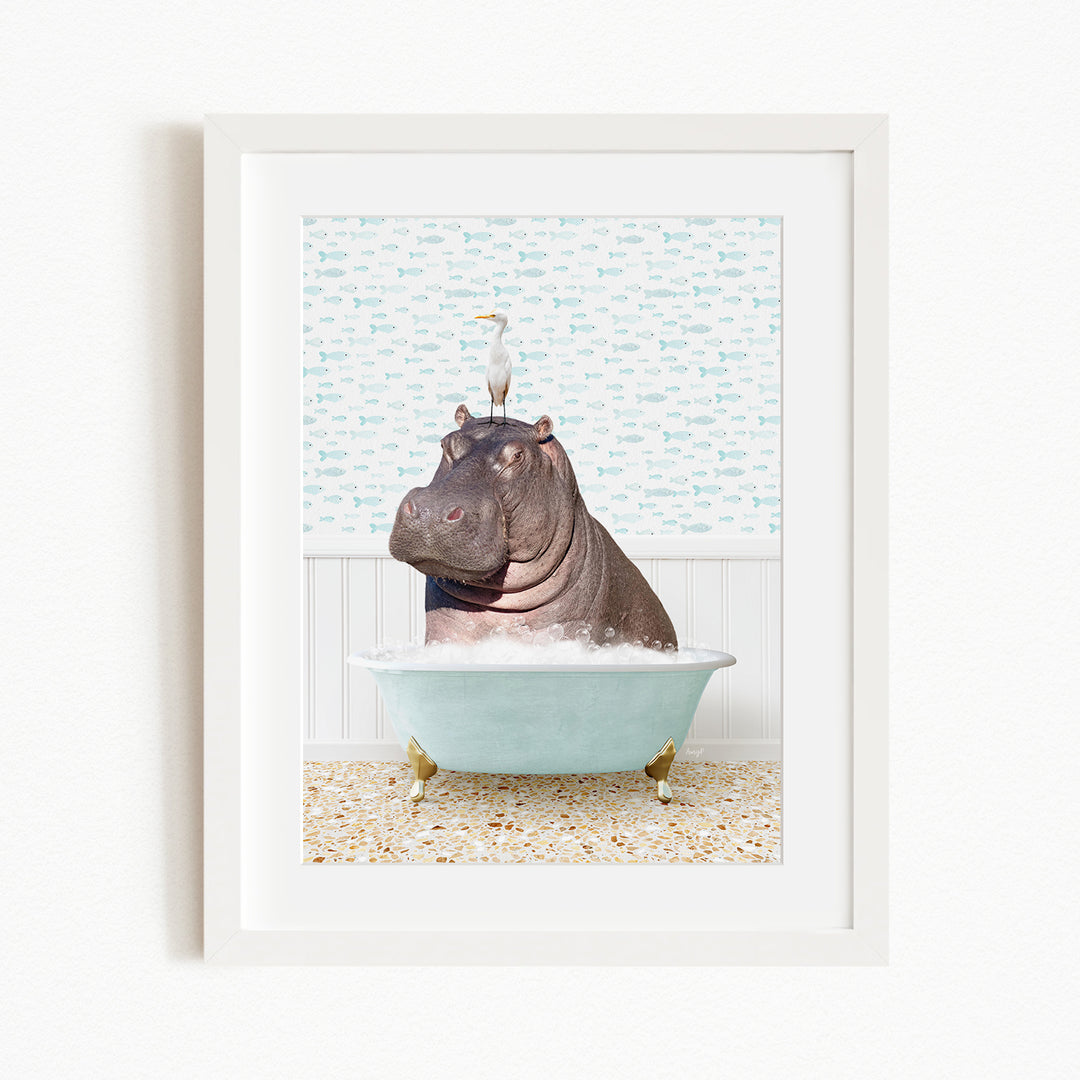 A framed image depicting a hippopotamus sitting in a bathtub, with a bird perched on its head.