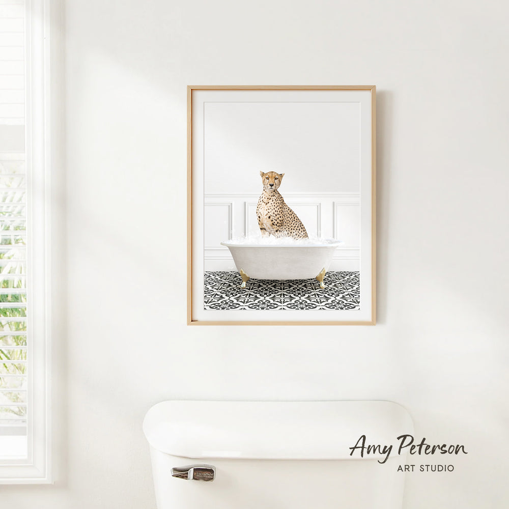A cheetah sitting in a white bathtub, with a patterned tile floor, is the central focus of the framed artwork displayed on the wall.