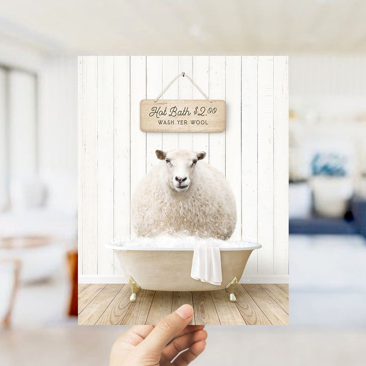 A hand holding a framed image of a sheep sitting in a bathtub, with a sign above it advertising a hot bath for $2.00.