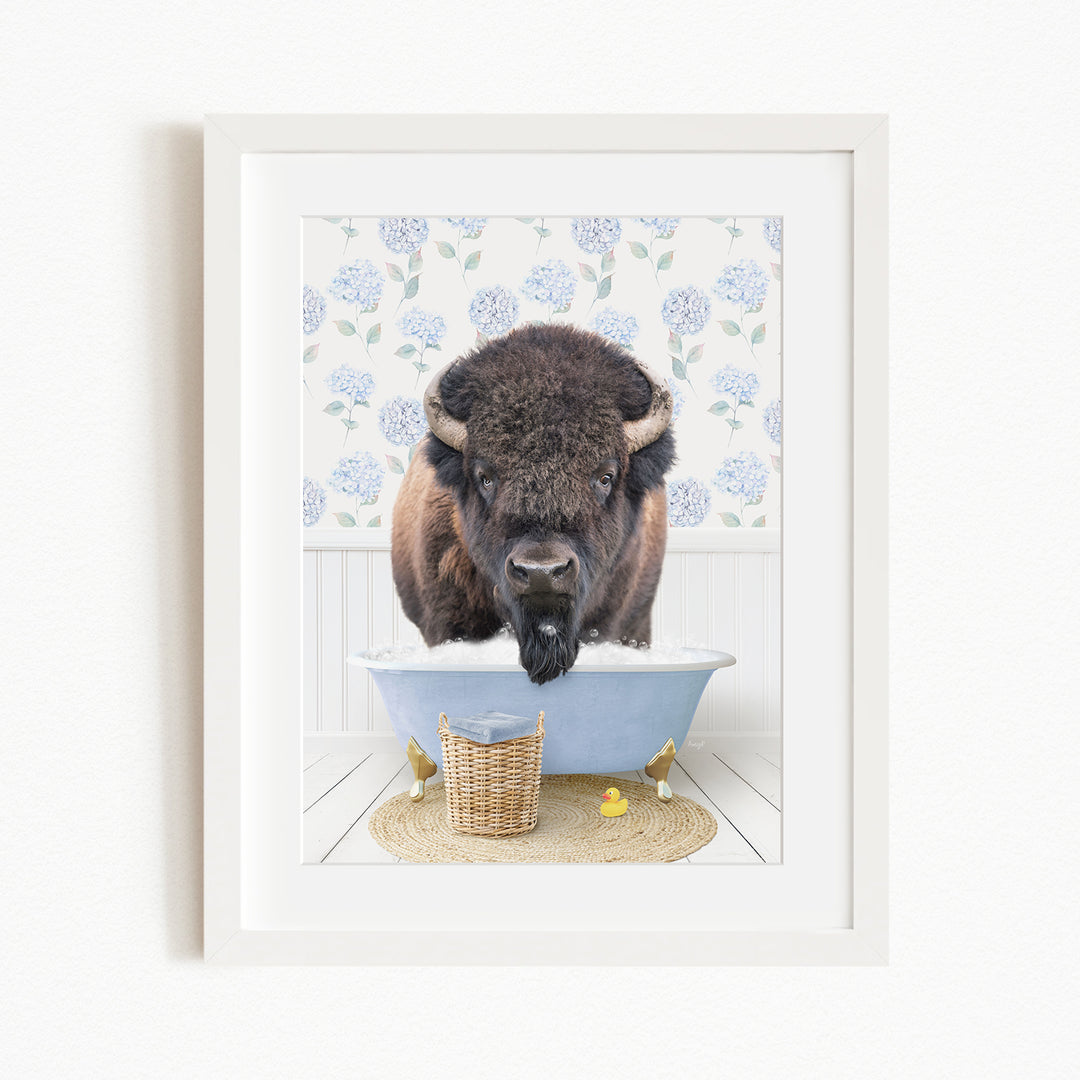A buffalo is standing in a blue bathtub filled with water, surrounded by yellow rubber ducks and a wicker basket.
