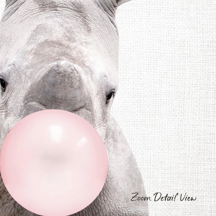 A close-up of a rhinoceros blowing a pink bubble with its mouth, against a plain white background.