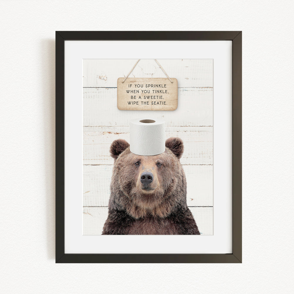 A framed image of a brown bear wearing a sign that says "If you sprinkle when you tinkle, wipe the seagrass"