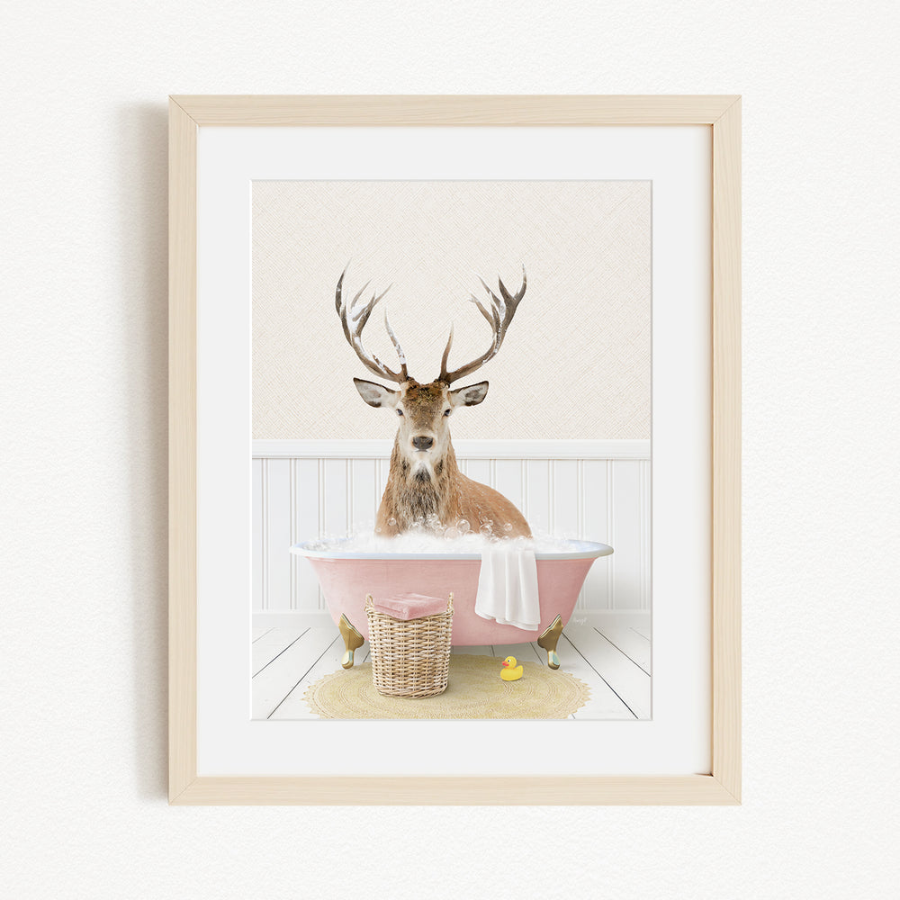 A deer with antlers is sitting in a pink bathtub filled with bubbles, surrounded by a yellow rubber duck and a basket.
