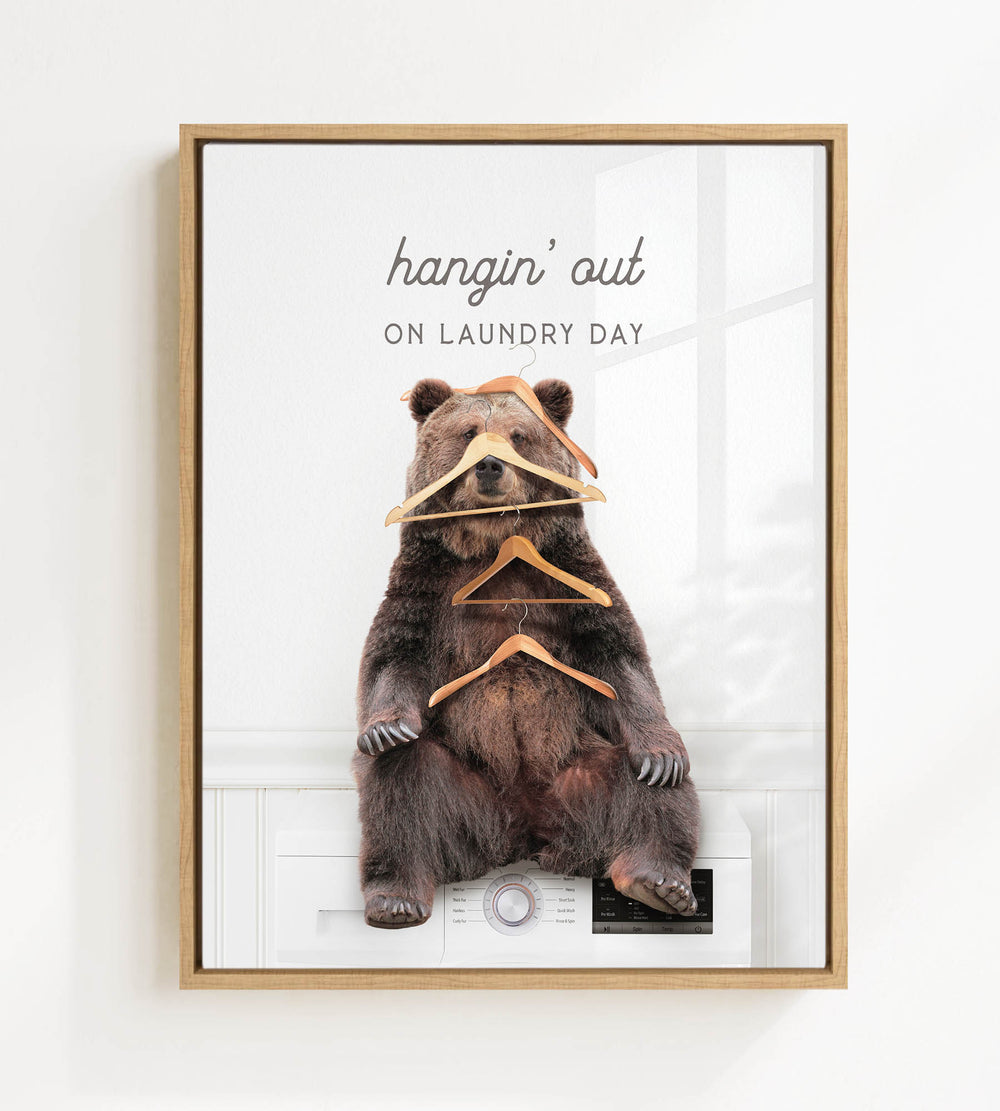 A brown bear sitting on a washing machine, surrounded by hanging clothes, with the text "hangin' out on laundry day" displayed above the bear.