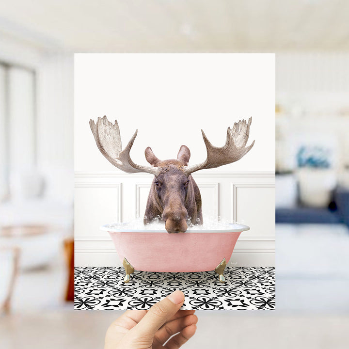 A moose with large antlers is sitting in a pink bathtub filled with water, creating a whimsical and humorous scene.