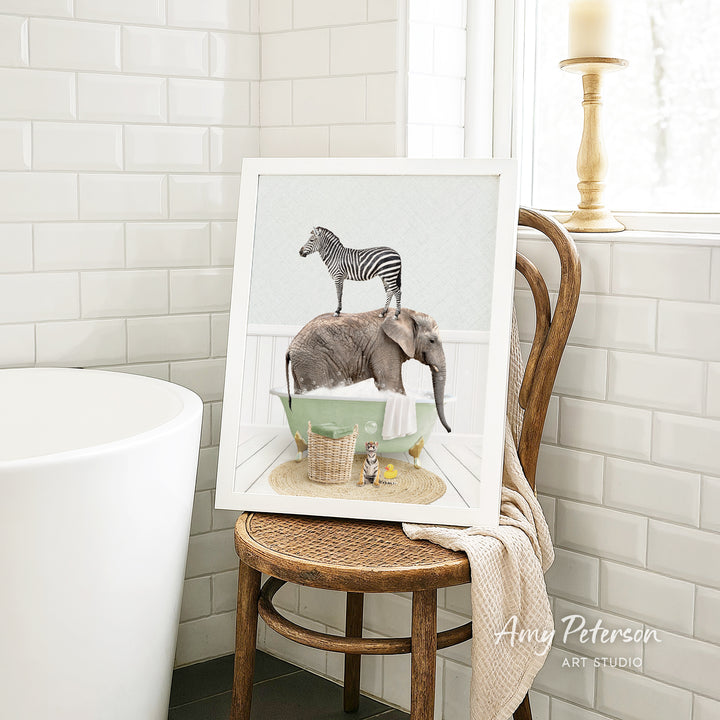 A framed image of a zebra standing on an elephant's back, with a green bathtub and a towel in the background, is displayed on a wooden chair in a bathroom setting.