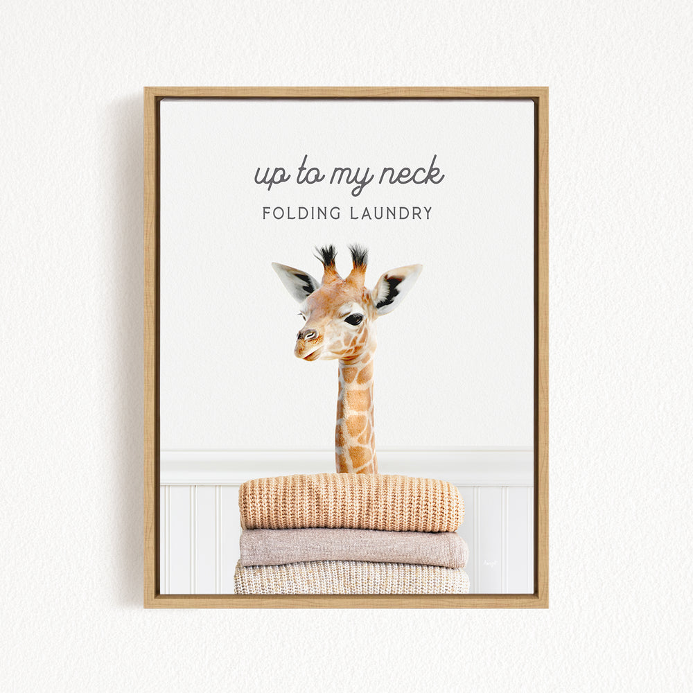 A framed image of a giraffe standing on a stack of folded towels, with the text "up to my neck" and "Folding laundry" written above it.