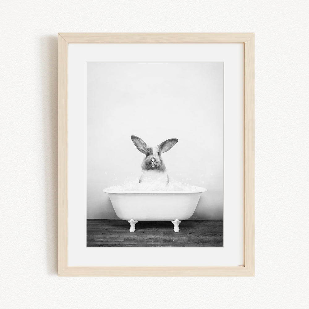 A black and white photograph of a rabbit sitting in a white bathtub filled with water, looking directly at the camera.