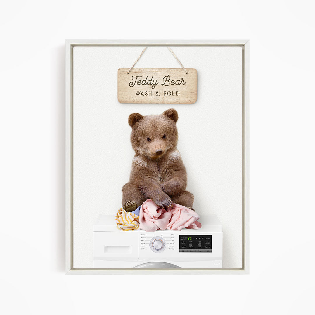 A teddy bear sitting on a pile of laundry inside a washing machine, with a sign above that says "Teddy Bear Wash & Fold".