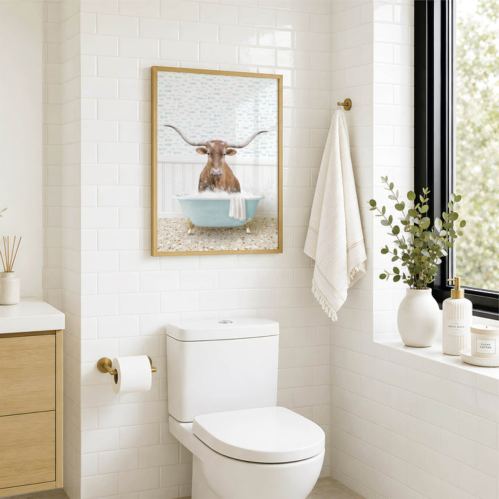 a bathroom with a white toilet, a framed picture of a bull in a bathtub, and a window with greenery outside.