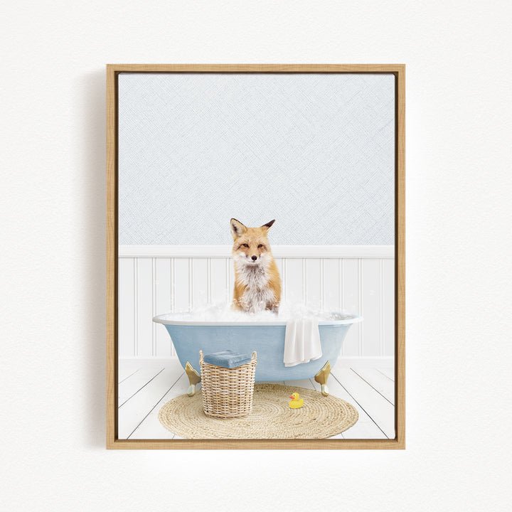A fox is sitting in a blue bathtub filled with bubbles, surrounded by a basket, a yellow rubber duck, and a white towel.