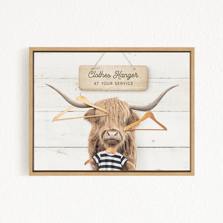 A wooden sign with the text "Clothes Hanger at your service" hangs above a large, furry animal with long horns, which appears to be a yak or a similar type of animal.