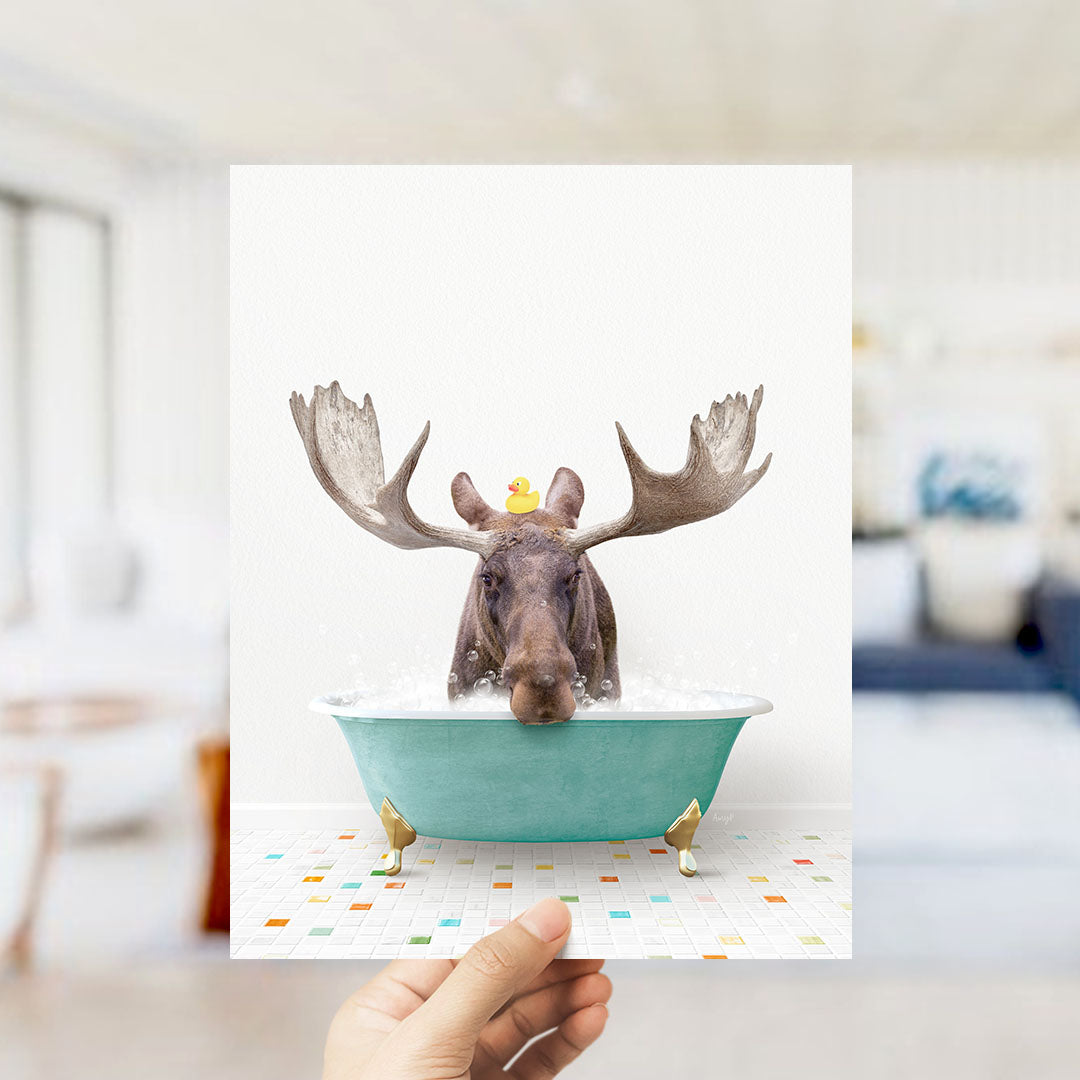 A moose with large antlers is sitting in a bathtub filled with bubbles, with a yellow rubber duck floating on its head.