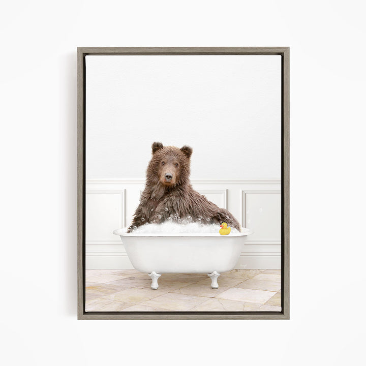 A brown bear sitting in a white bathtub, with a rubber duck floating in the water.