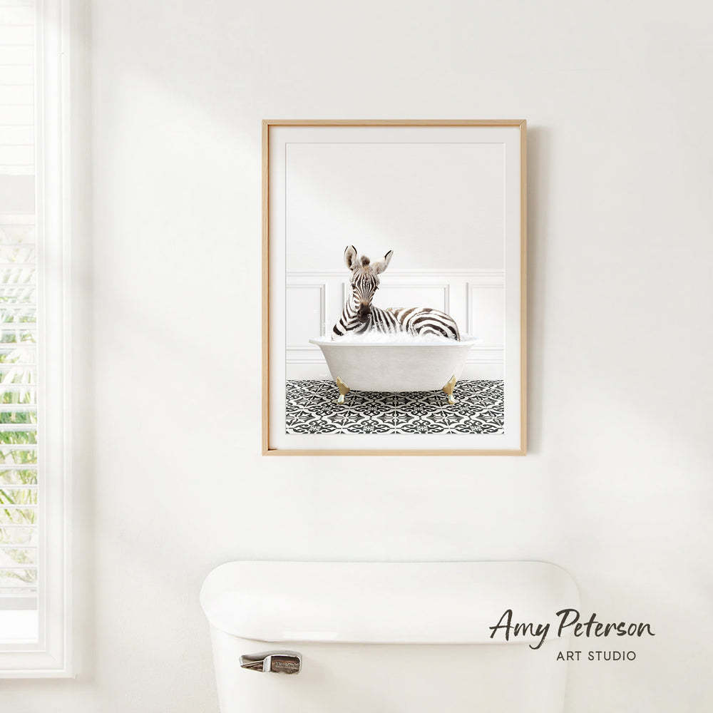 A framed image of a zebra sitting in a bathtub is hanging on a white wall in a bathroom.