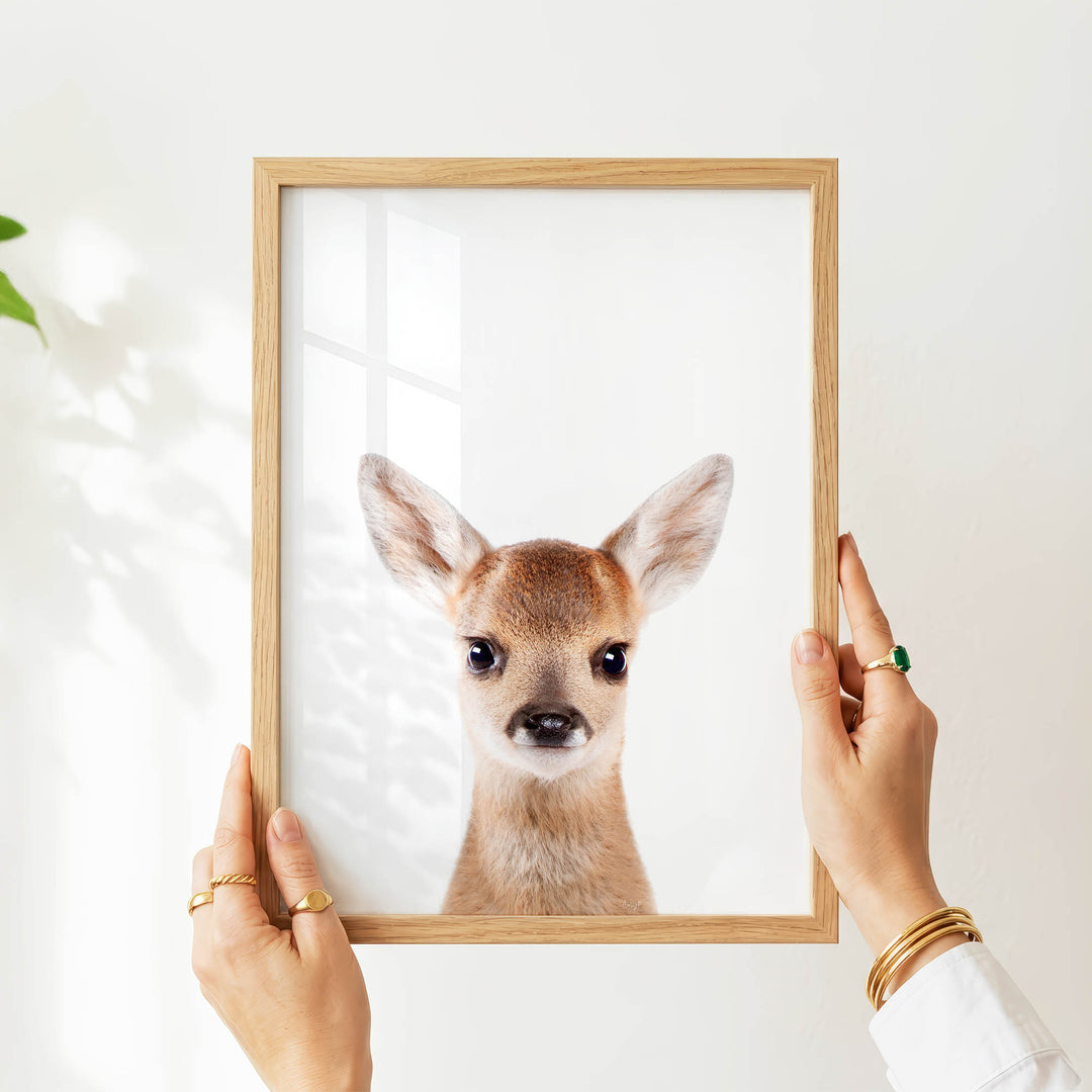 A person's hands are holding a wooden frame with a picture of a deer inside it.