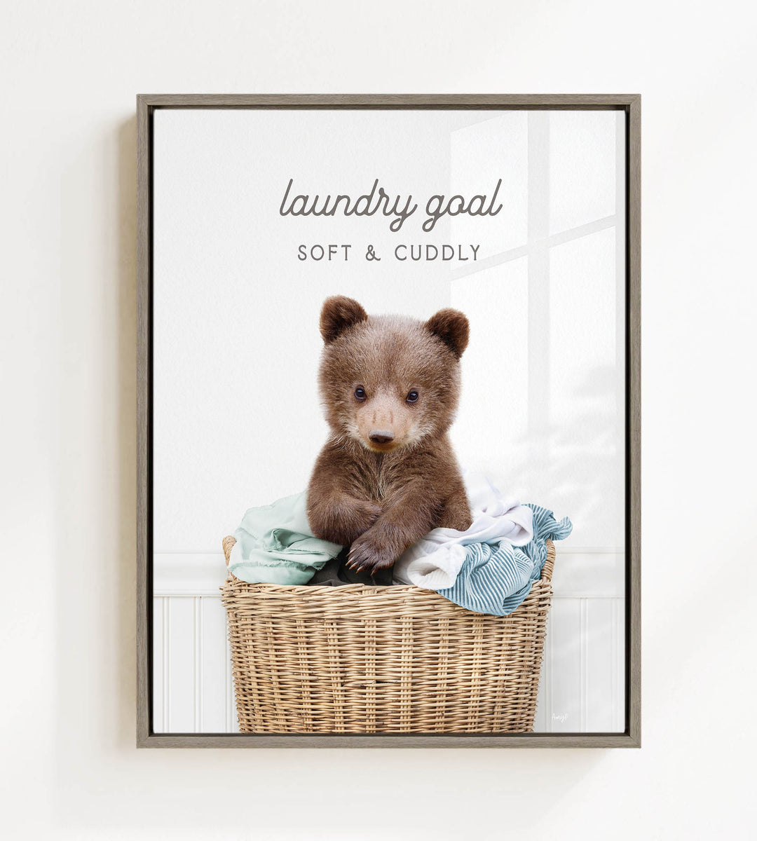 A cute brown bear sitting in a wicker laundry basket filled with clothes, with the text "laundry goal" and "soft & cuddly" written above it.