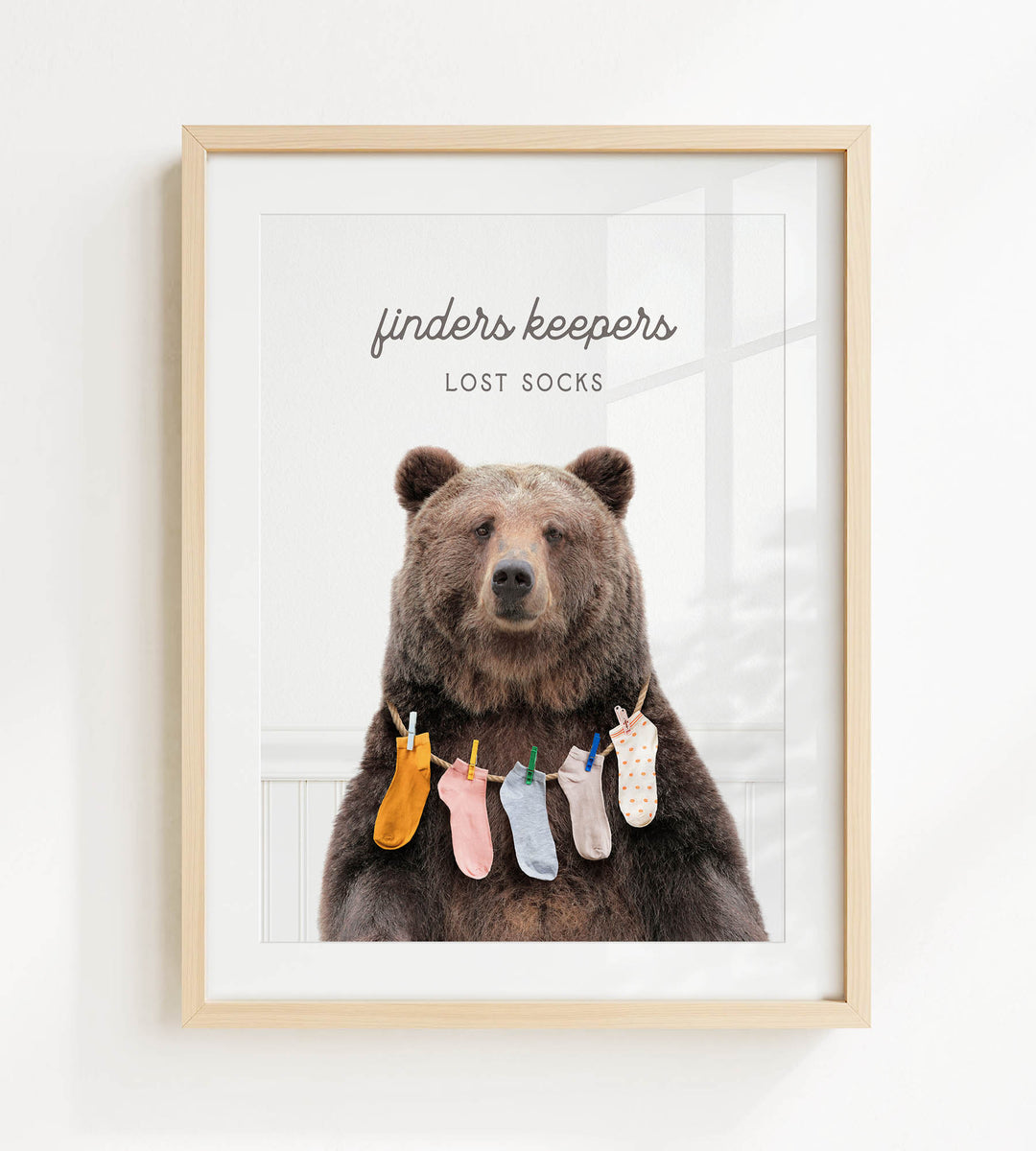 A framed image of a brown bear wearing a variety of colorful socks hanging from clothespins.