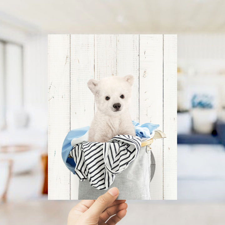 A small white polar bear cub sitting in a basket filled with clothes.