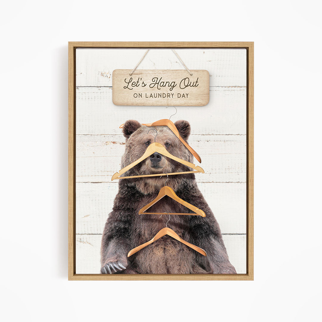 A framed image of a bear holding multiple wooden hangers, with a sign above that says "Let's Hang Out on laundry day".