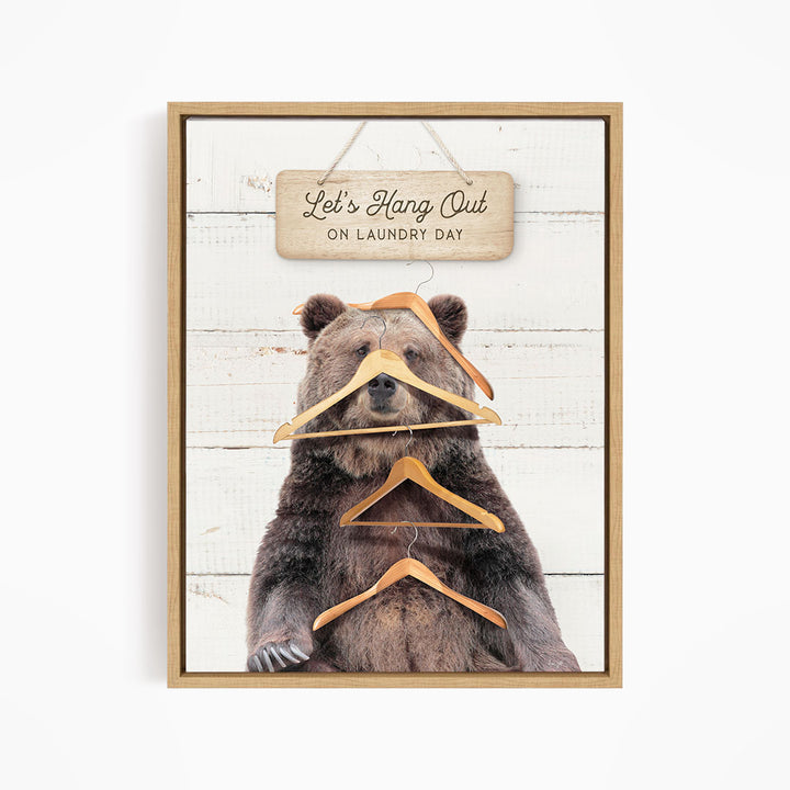 A framed image of a bear holding multiple wooden hangers, with a sign above that says "Let's Hang Out on laundry day".