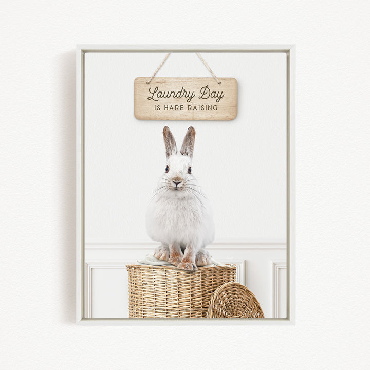 A white rabbit sitting on a woven basket, with a wooden sign above that says "Laundry Day is HARE RAISING".
