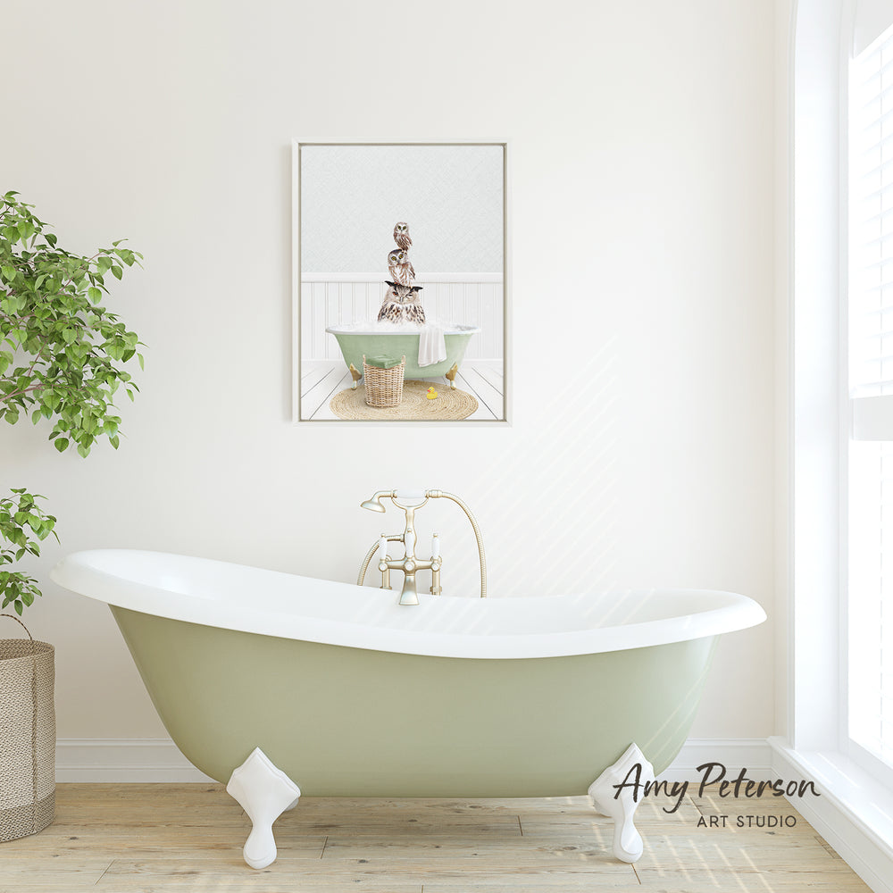 A green clawfoot bathtub sits in a bright, airy bathroom, with a framed image of a person sitting in the tub above it.