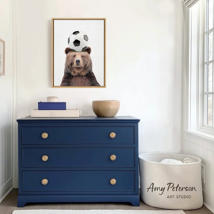 a blue dresser with a framed picture of a bear balancing a soccer ball on its head. The dresser is situated in a room with white walls and a window.
