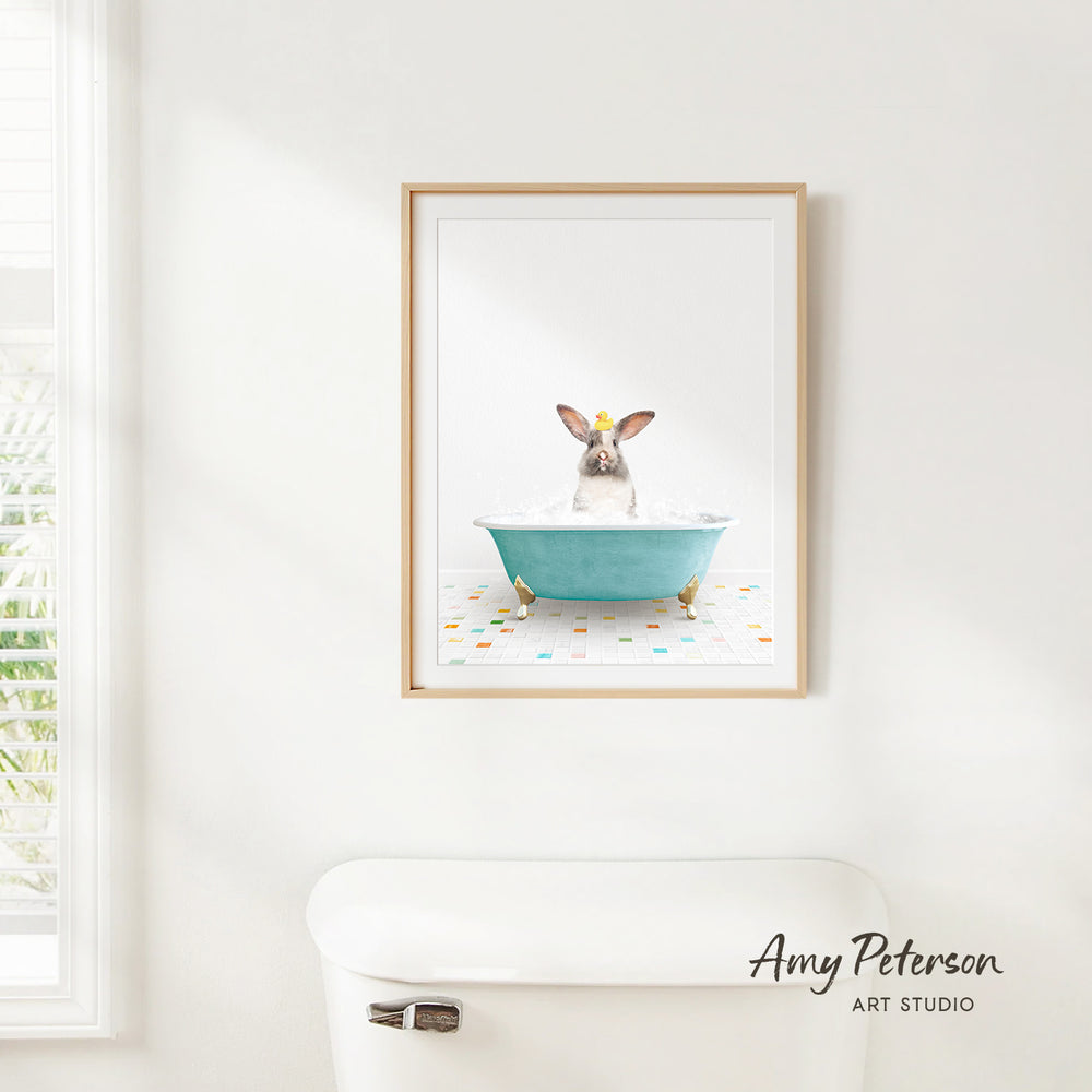 A framed image of a rabbit sitting in a blue bathtub, with a white toilet and a window in the background.
