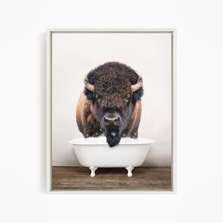 A bison with large horns is standing in a white bathtub, appearing to be enjoying a bath.