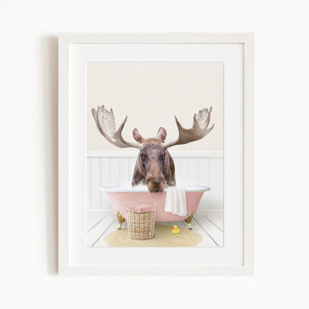 A moose with large antlers is sitting in a pink bathtub, surrounded by a yellow rubber ducky and a basket.
