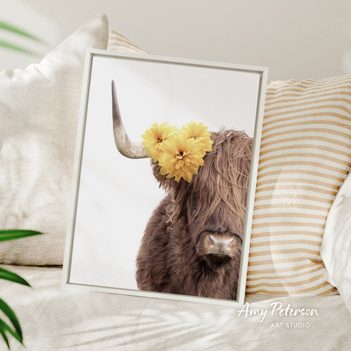 A framed photograph of a brown cow with yellow flowers on its horns, placed on a white pillow.