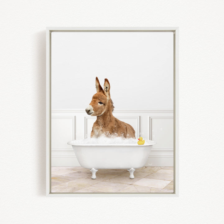 A donkey is sitting in a white bathtub filled with bubbles, with a rubber duck floating in the water.