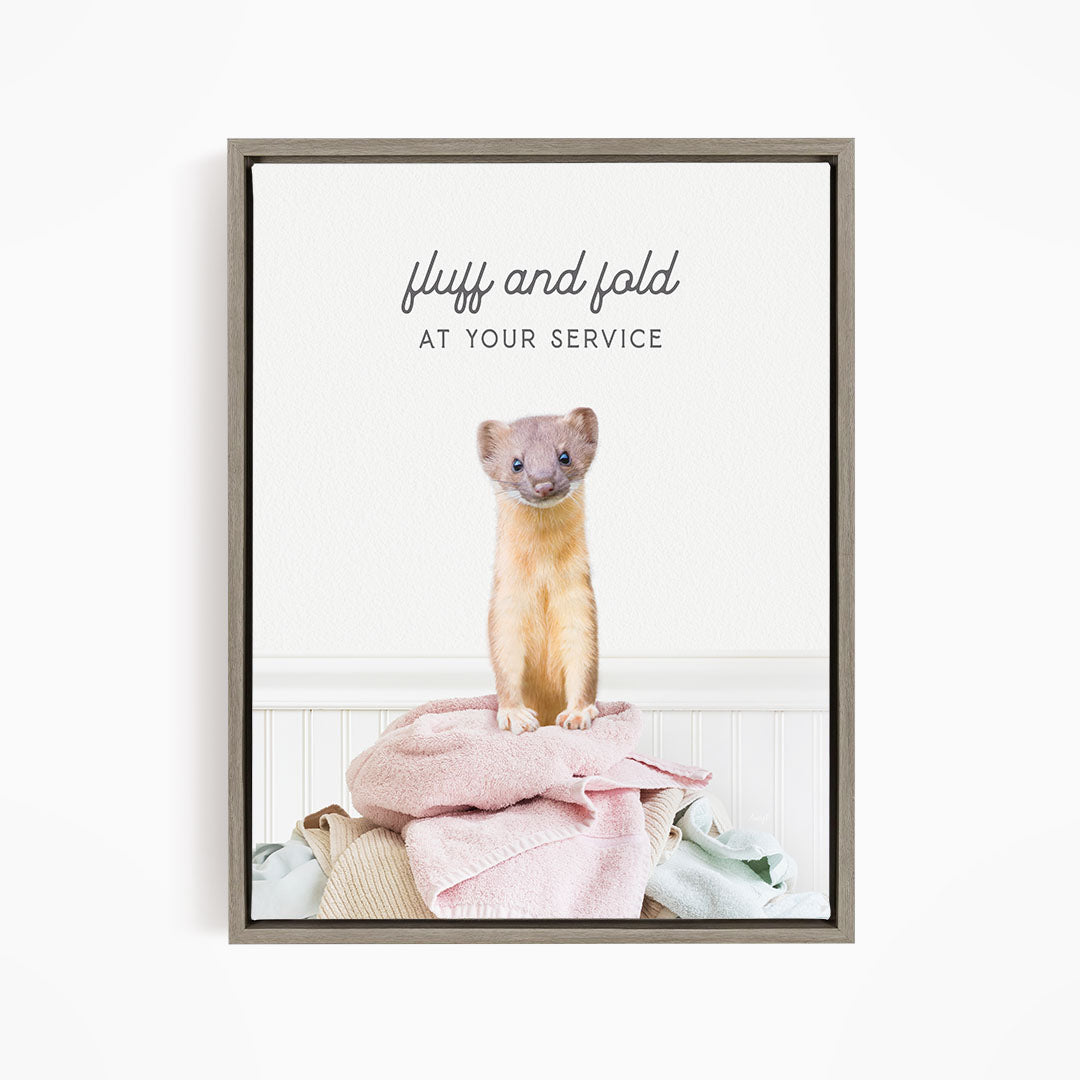 A small brown and white ferret sitting on a pile of clothes, with the text "fluff and fold at your service" written above the image.