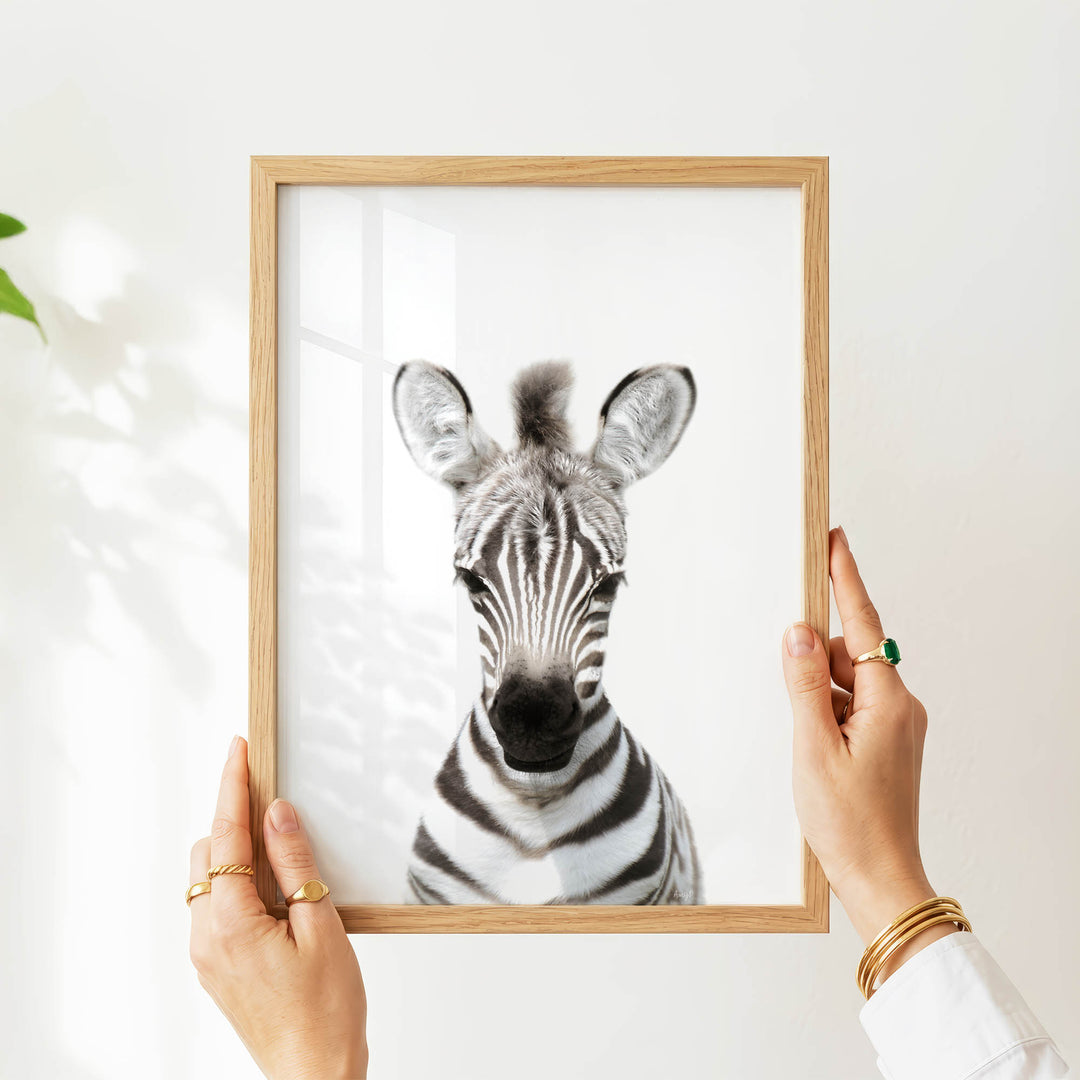 A person's hands are holding a wooden frame with a picture of a zebra inside it.