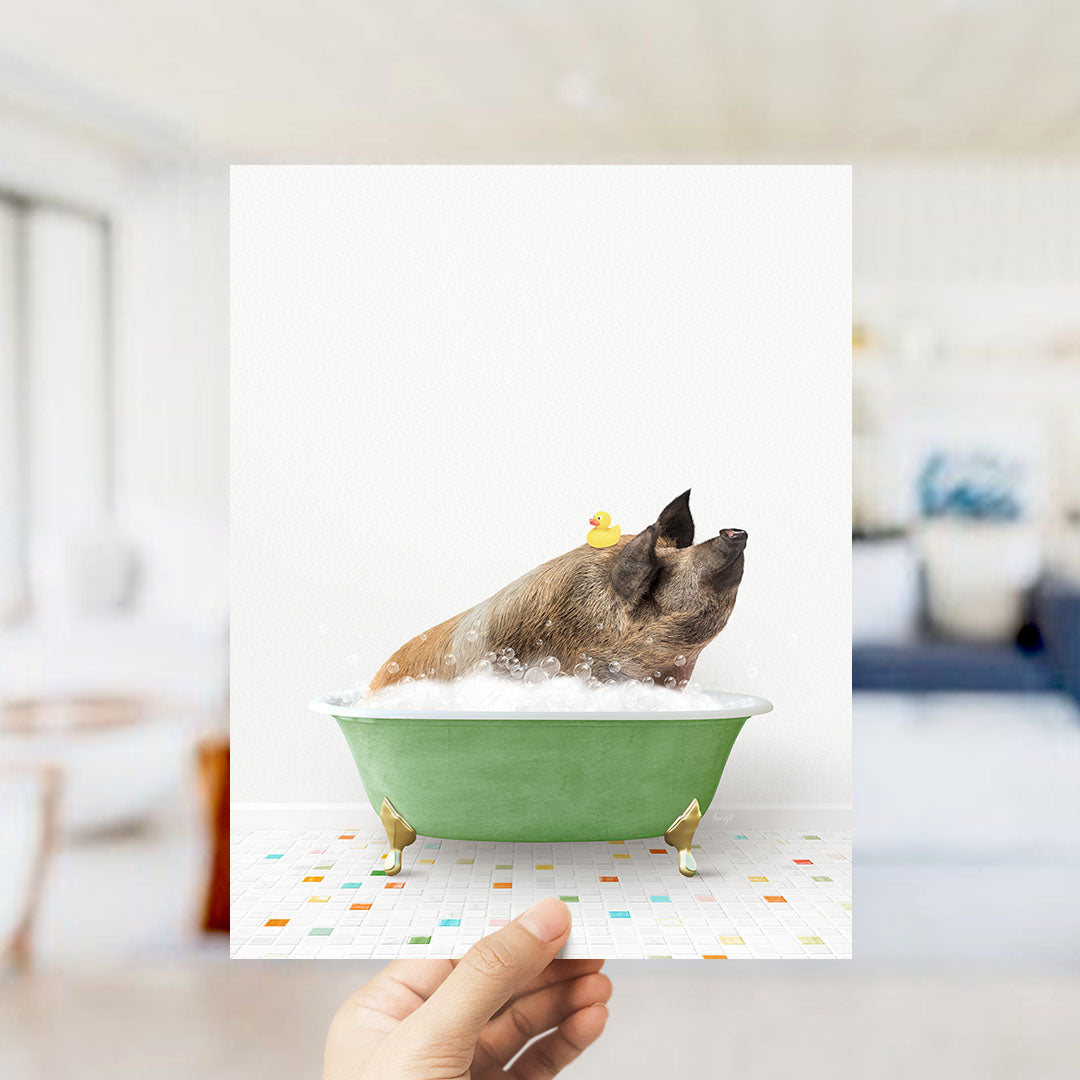 A hand holds up a framed image of a pig sitting in a green bathtub, surrounded by bubbles and a rubber duck.