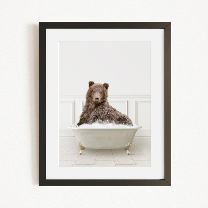 A brown bear sitting in a white bathtub filled with water, looking directly at the camera.