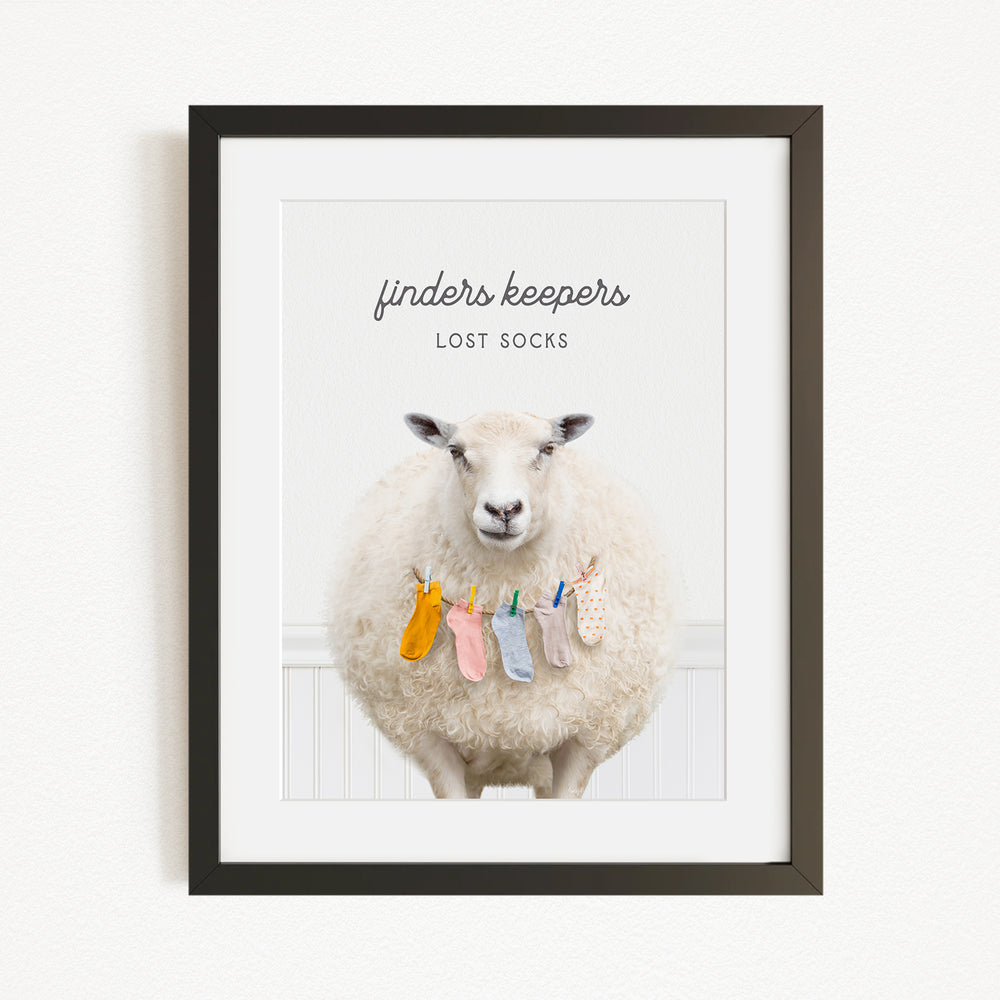 A framed image of a sheep wearing a pile of colorful socks, with the text "finders keepers" and "lost socks" above the sheep.