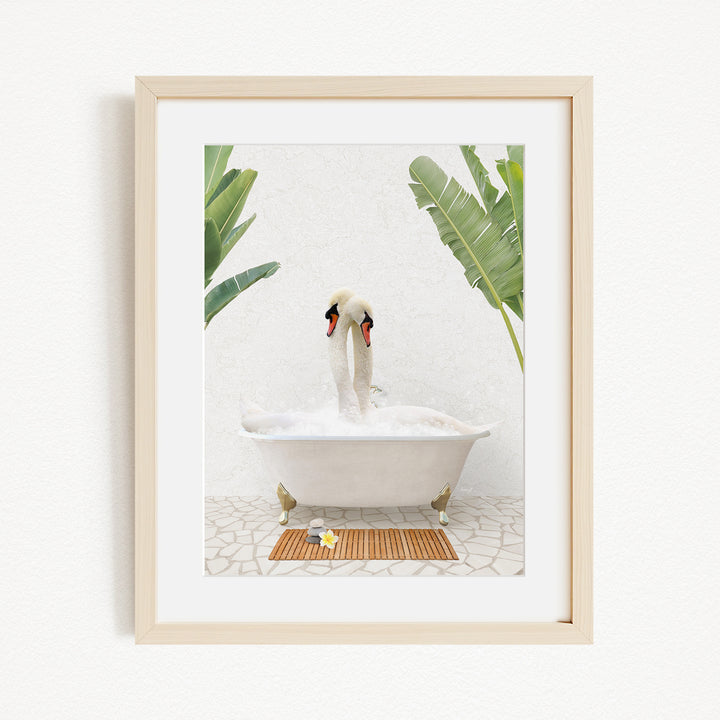 A white swan is sitting in a white bathtub filled with bubbles, surrounded by green plants and a wooden mat on the floor.