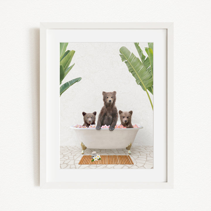 A framed image depicting three bears sitting in a bathtub filled with pink flowers, surrounded by green plants.