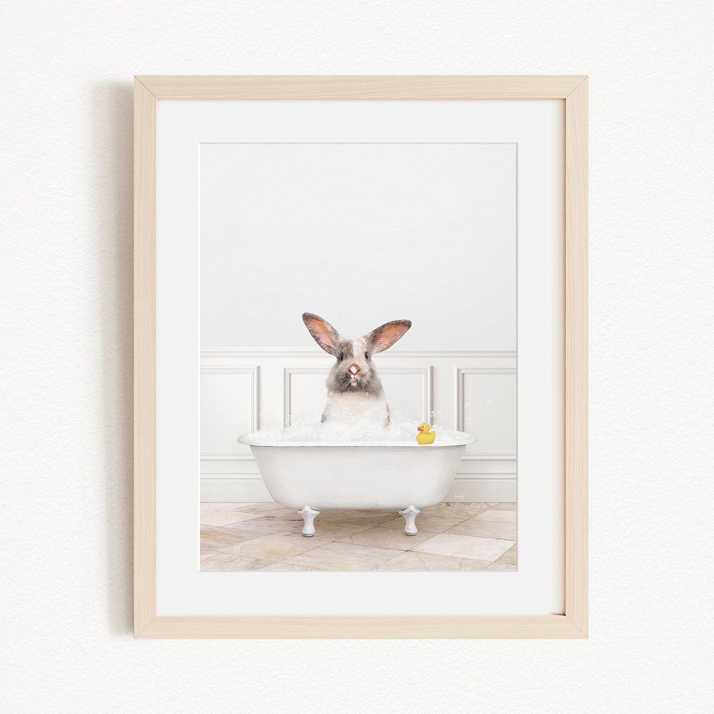 A white rabbit sitting in a white bathtub filled with bubbles, with a yellow rubber duck floating in the water.