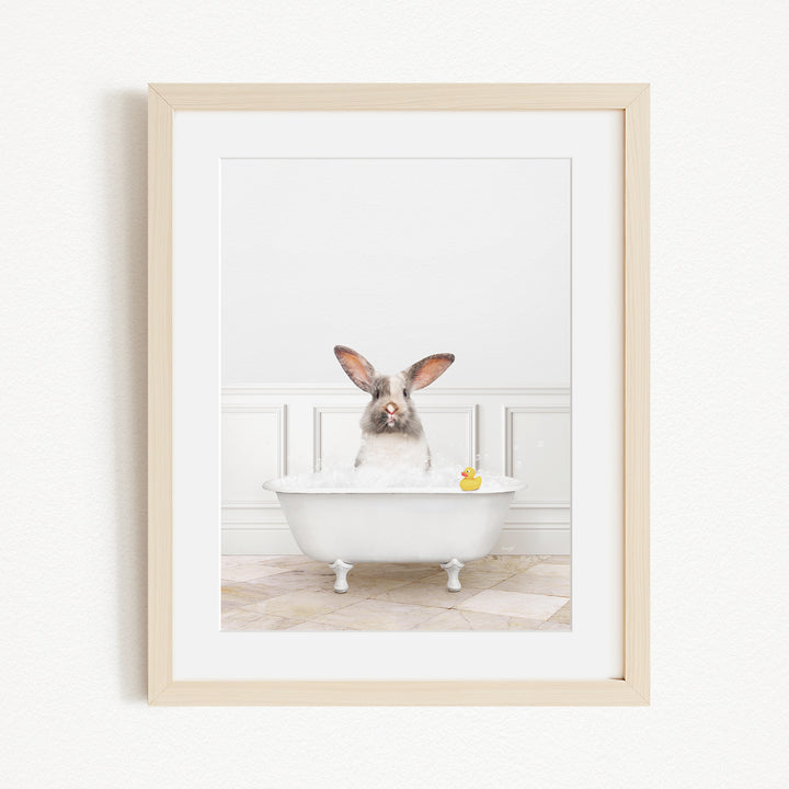 A white rabbit sitting in a white bathtub filled with bubbles, with a yellow rubber duck floating in the water.